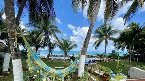 Un hamac tendu entre deux palmiers, avec vue sur une plage et un ciel dégagé.
