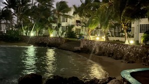 Un hôtel situé en bord de mer, agrémenté de palmiers, doté d’une piscine et d’un mur en pierre.