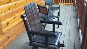 Een houten terras met schommelstoelen en een overdekt gedeelte met houten balustrade.