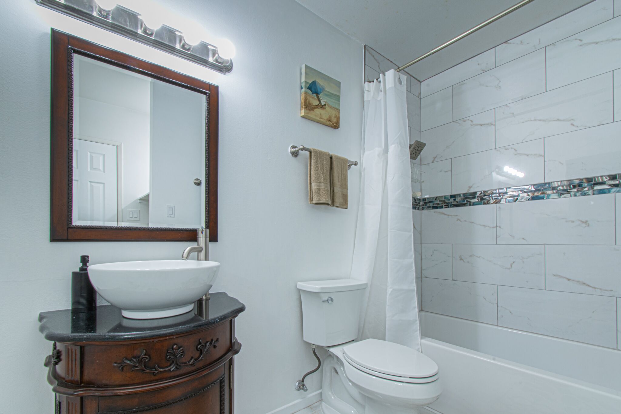 Een badkamer met een witte wastafel, een houten opbergmeubel, een wit toilet, een douche met een witte douchegordijn en een spiegel met houten lijst.