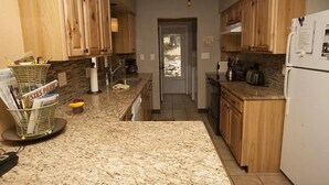 A kitchen with wooden cabinets, granite countertops, and a refrigerator. - Steps away from Wild Basin:RMNP- 2-bdrm cabin perfect for adventure or relaxing! (Allenspark)