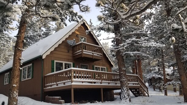 A wooden cabin with a balcony, surrounded by snow-covered trees. - Steps away from Wild Basin:RMNP- 2-bdrm cabin perfect for adventure or relaxing! (Allenspark)