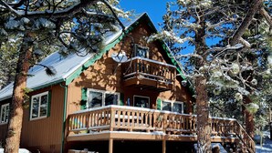 A wooden cabin with a balcony, surrounded by snow-covered trees. - Steps away from Wild Basin:RMNP- 2-bdrm cabin perfect for adventure or relaxing! (Allenspark)