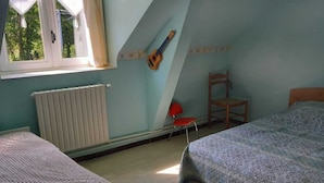 A room with two beds, a window with curtains, a guitar, a radiator, and a chair. - Gîte à la Campagne "beauregard" à LA Fleche (La Flèche)