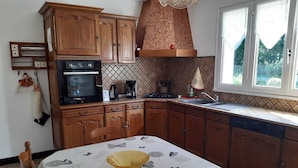 A kitchen with wooden cabinets, a built-in oven, a coffee maker, and a window with a view of greenery. - Gîte à la Campagne "beauregard" à LA Fleche (La Flèche)