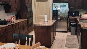 Cozinha com armários de madeira escura, geladeira de aço inoxidável e área de jantar com mesa posta para quatro pessoas.