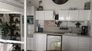 Une cuisine moderne avec des armoires blanches, un four à micro-ondes encastré, une machine à café et un coin repas comprenant une table et des chaises de couleur marron.