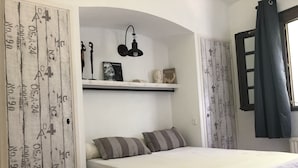 Une chambre à coucher avec un lit, des oreillers, une étagère décorative et une fenêtre avec des rideaux.