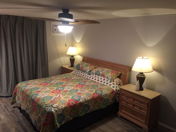 A bedroom with a bed, two bedside tables with lamps, a ceiling fan, and a window with curtains.