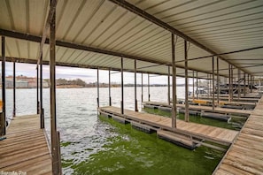Boats dock beneath a sheltered structure supported by metal beams and columns.