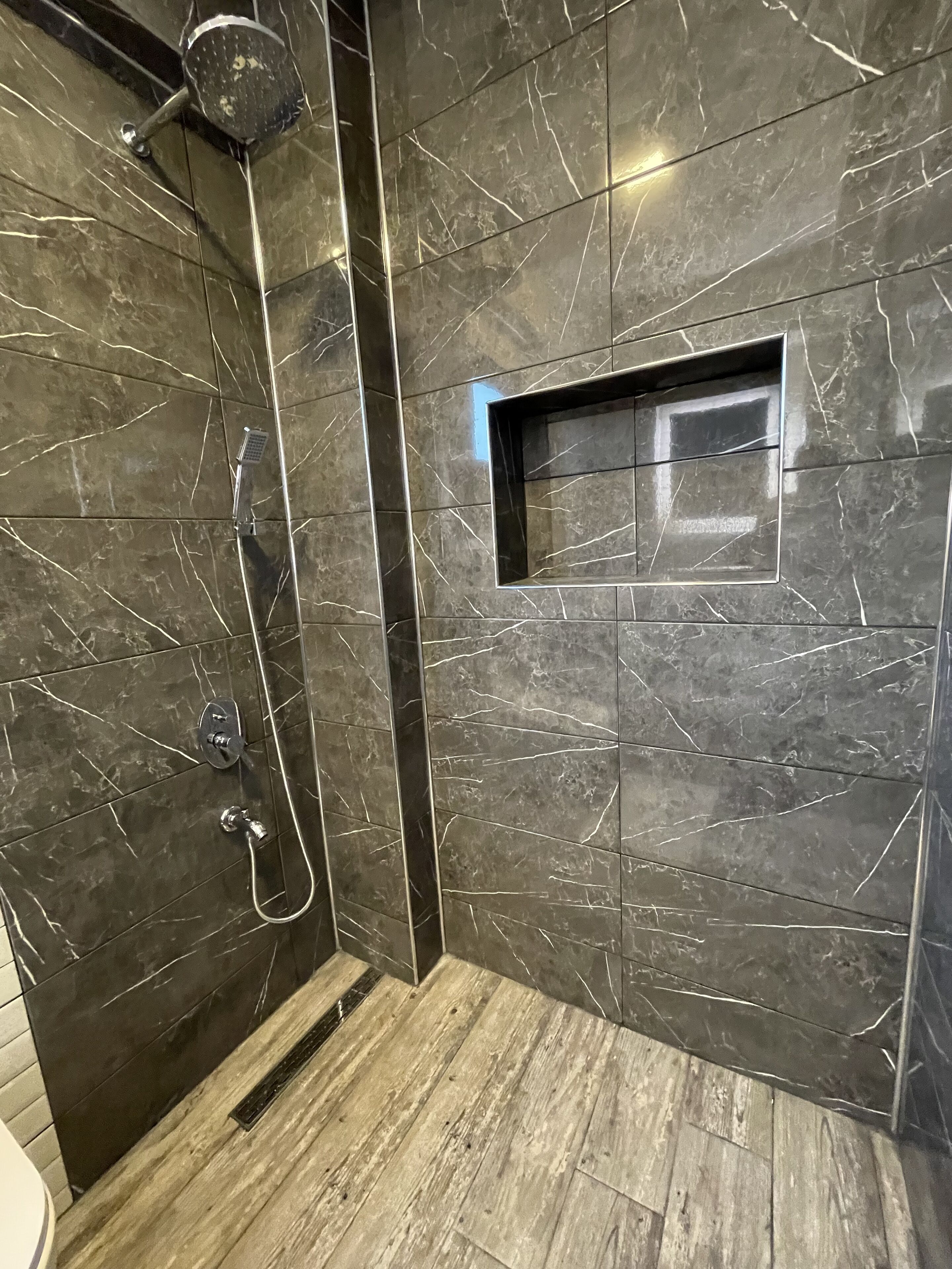 Un baño moderno con paredes de mármol oscuro, zona de ducha y suelo de madera.