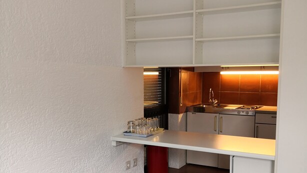 Habitació senzilla amb llit, cuina americana i menjador petit.