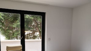 Habitació amb llit, cadira, taula petita i finestra amb vista als arbres.
