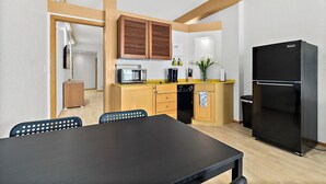 Uma cozinha compacta com armários de madeira, uma geladeira preta e um espaço de refeições com mesa e cadeiras.