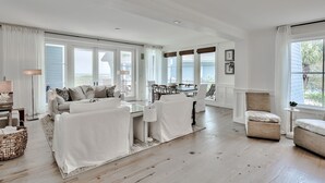 A spacious living room with a large window, a dining area, and a cozy seating area. - Direct Beach/Pool Access from Watersound Condo - Comp Bikes, Boards, Beach Gear! (Watersound)