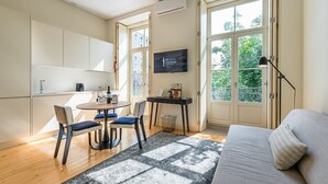 Ett modernt vardagsrum med en soffa, ett matbord med stolar, en tv och ett stort fönster med utsikt över grönområden.