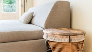 En beige soffa med en kudde och ett flätat sidobord.