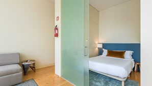 Ett hotellrum med en säng, en soffa, ett litet bord och en glasvägg.
