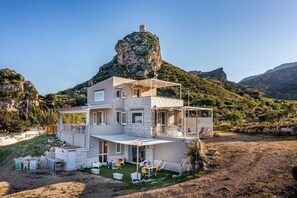 Una casa de dos pisos con un patio, una piscina pequeña y vistas a una colina rocosa.