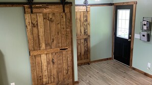 Um quarto com soalho de madeira, uma porta preta com janela e um teto com vigas à vista.
