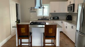 Une cuisine moderne dotée d’un îlot central, d’appareils électroménagers en acier inoxydable et de chaises en bois.