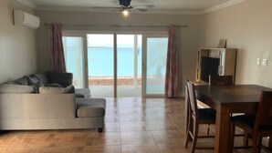 Un salon avec un canapé, une table à manger et des chaises, et une vue sur la mer grâce à de grandes portes vitrées.
