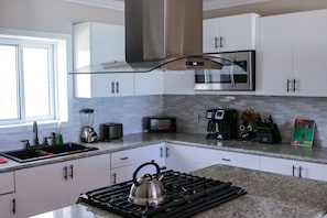 Una cocina moderna con armarios blancos, una campana extractora de acero inoxidable, una estufa a gas, una licuadora, un tostador y una cafetera.