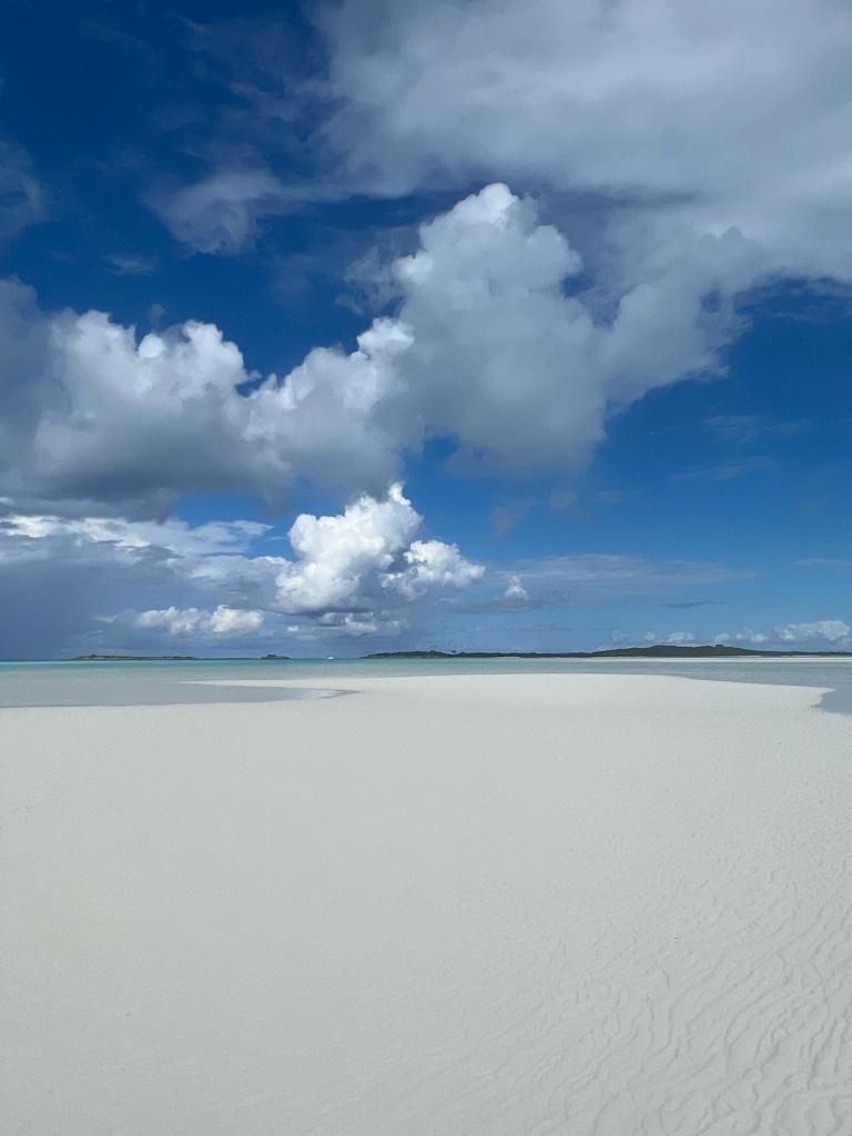 A vast, white sandy beach with a clear sky and scattered clouds.