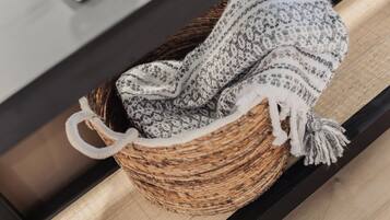 A woven basket with a crocheted blanket and a tassel, placed on a wooden surface.