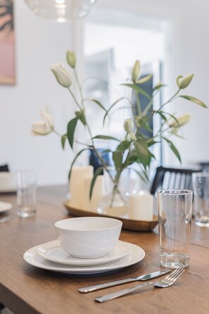 A dining table with a white bowl, plates, cutlery, and a clear glass. There is a vase with green leaves and white buds in the background. - Shuffleboard/Swimming Pool/BBQ Grill, 4 Miles To The Strip, Pet Friendly! (Las Vegas)