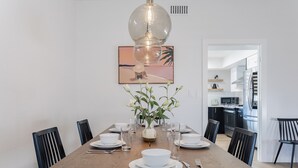 A dining table set with white plates, bowls, and cutlery, surrounded by black chairs. A vase with green plants is placed in the center. - Shuffleboard/Swimming Pool/BBQ Grill, 4 Miles To The Strip, Pet Friendly! (Las Vegas)