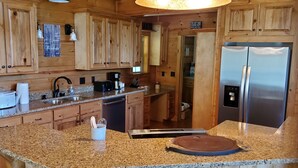 Una cocina con armarios de madera, encimeras de granito, un refrigerador de acero inoxidable y una cafetera.