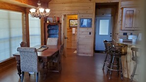 Un interior de madera con una mesa de comedor, sillas, una araña y una zona de cocina con taburetes de bar.