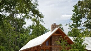 Una cabaña rústica de madera con techo metálico, rodeada de abundante vegetación y árboles.