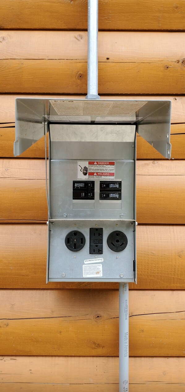 Una caja eléctrica metálica fijada a una pared de madera con dos enchufes y una etiqueta de advertencia.