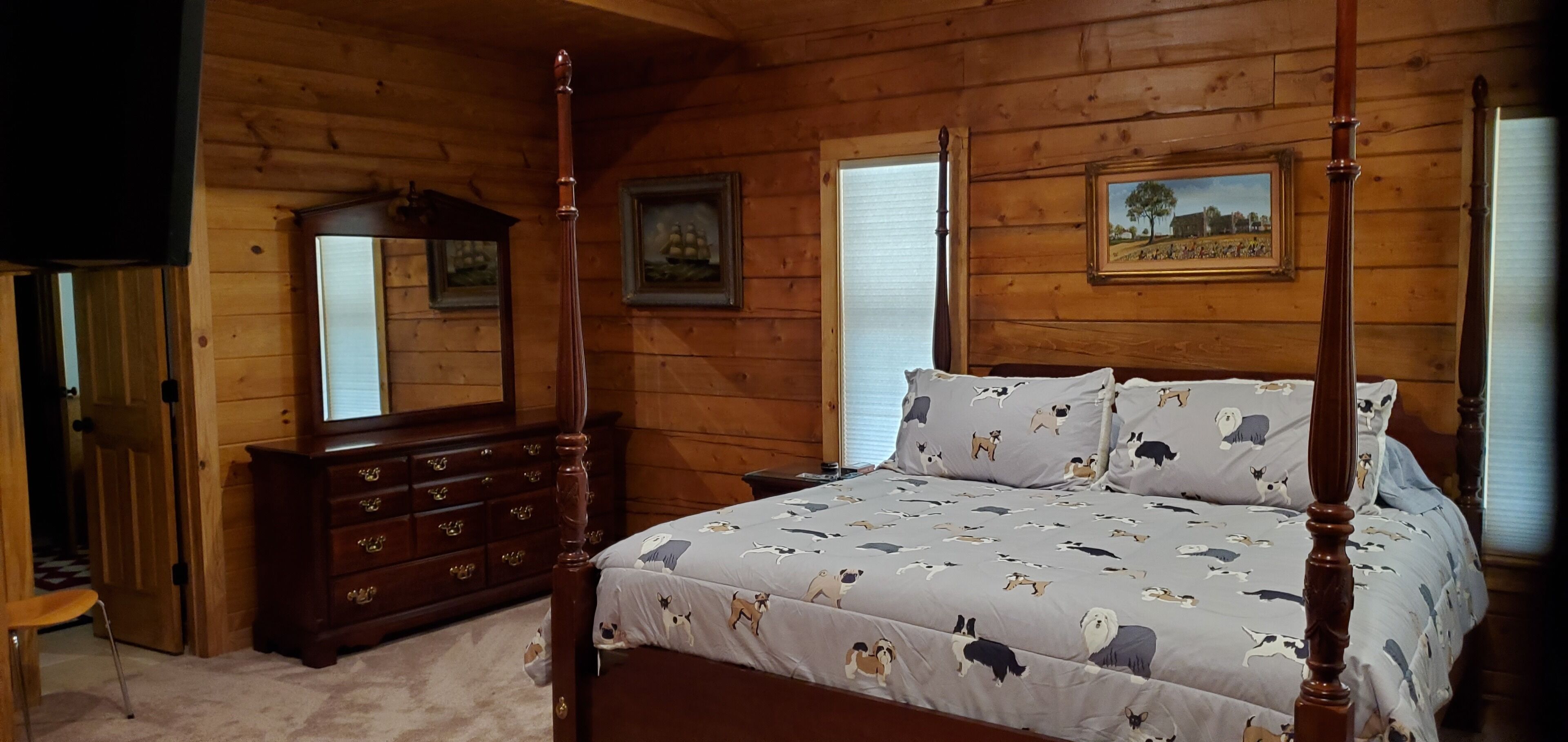A wooden-paneled bedroom with a four-poster bed, a dresser, and two framed pictures on the wall.