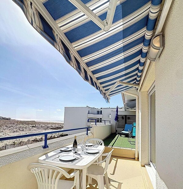 A balcony with a table set for dining, a chair, and a bottle of wine.
