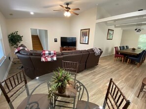 A living room with a sectional sofa, a glass dining table, and a ceiling fan.
