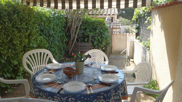 Un patio al aire libre con una mesa redonda lista para comer, rodeada de sillas blancas, bajo un toldo a rayas.
