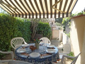 An outdoor patio with a round table set for dining, surrounded by white chairs, under a striped awning. - Pleasant 2 room mezzanine Mt St Martin Cap d'Agde (LE CAP D'AGDE)