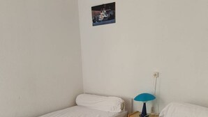 Una habitación pequeña y sencilla con dos camas individuales, una mesita de noche con lámpara y un cuadro pequeño en la pared.