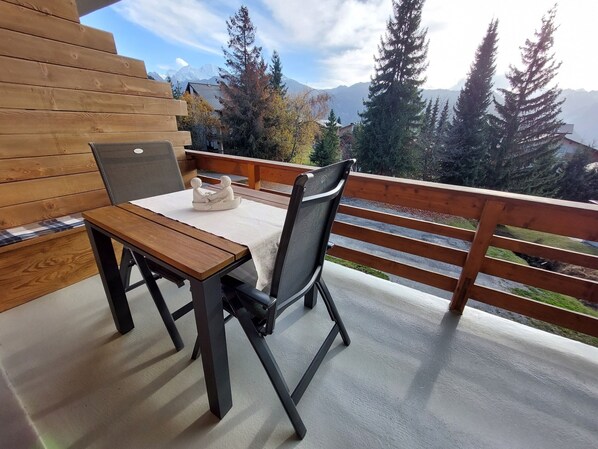 Una terraza de madera con una mesa y sillas, con vistas a un paisaje montañoso.