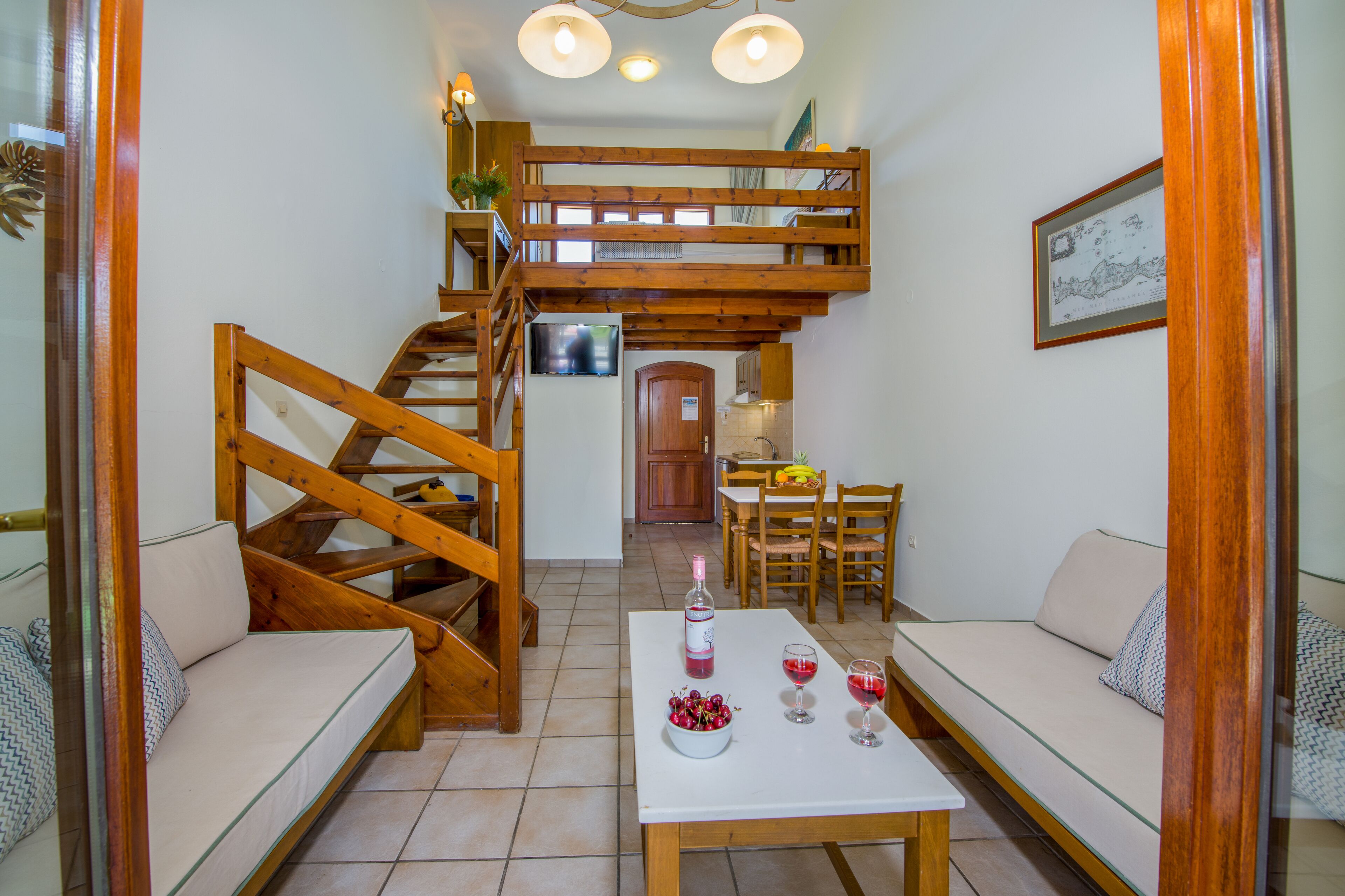 Un salon chaleureux avec un escalier en bois, un coin repas et une cuisine en arrière-plan.