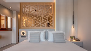 Una habitación de hotel moderna con una cama grande, un panel de madera decorativo, una mesita de noche con lámpara y otra mesita con un teléfono y una planta.
