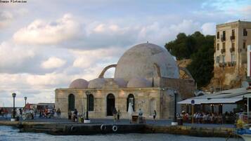 A waterfront building with a large dome and multiple smaller domes, a stone facade, and a port with boats.