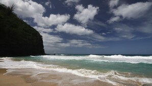 A beach with waves, a cliff, and a partly cloudy sky. - Ocean Front Condo with AC, enjoy the ocean from your own private lanai. (Koloa)