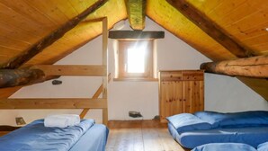 A cozy attic bedroom with two beds, wooden beams, a small window, and a wooden wardrobe. - Rustico Dolomia by Interhome (Olivone)