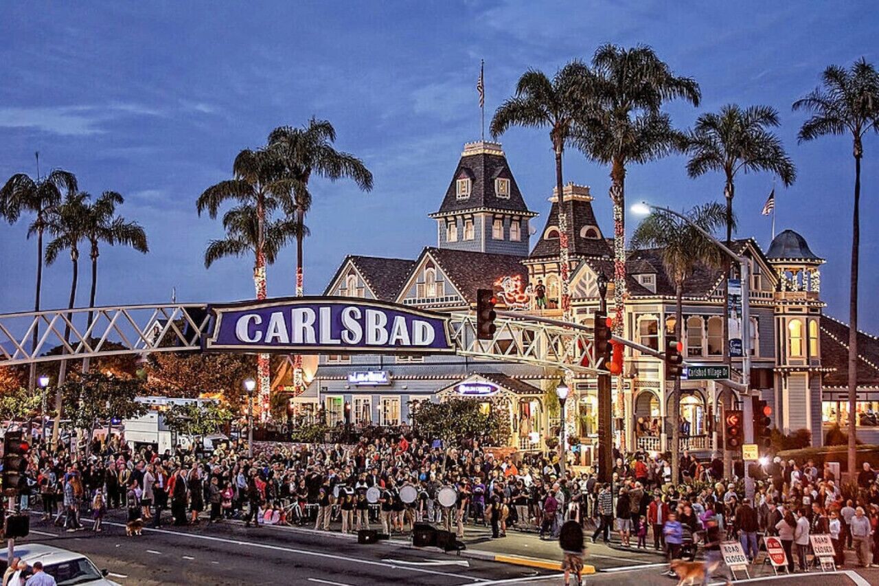 Une rue animée où une foule nombreuse s’est rassemblée devant un bâtiment historique portant l’inscription « CARLSBAD ».