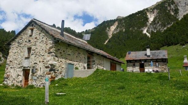 Ein Steinhaus mit einem geneigten Dach, einem Schornstein und einem kleinen Anbau.