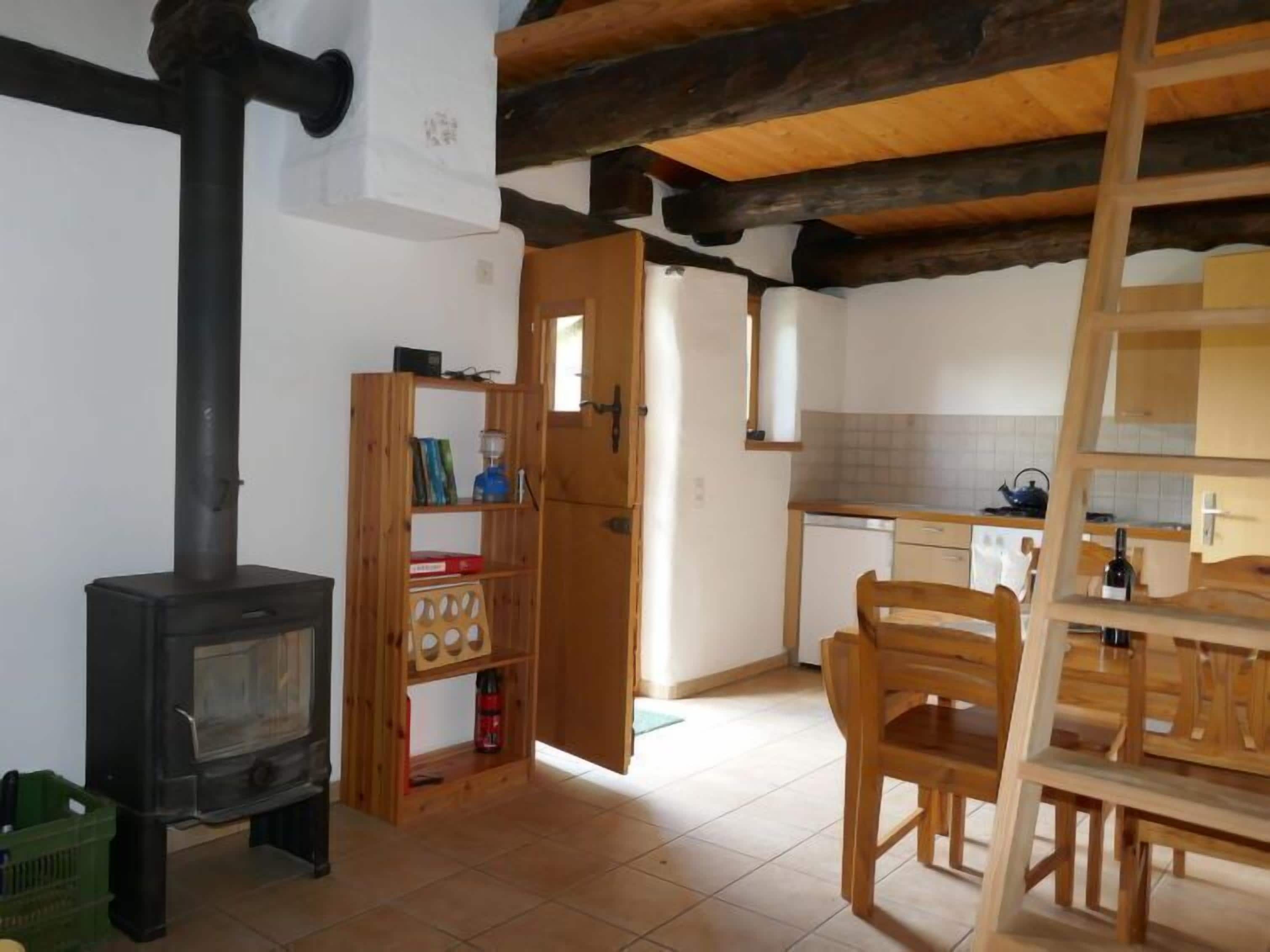 A rustic kitchen with a wood stove, a wooden bookshelf, and a dining area with chairs.